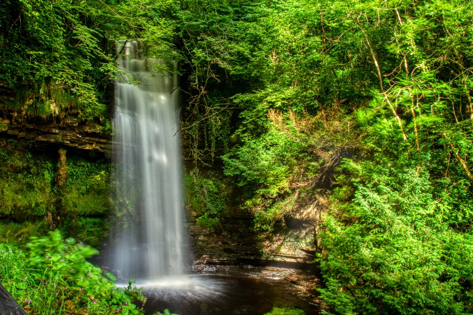 Stunning long exposure of a waterfall surrounded by vibrant greenery in a serene Irish forest.